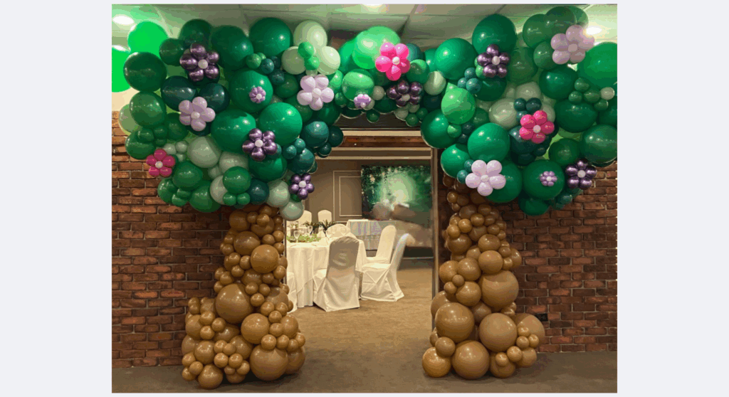 Image of balloon arch resembling two trees with flowers that frames the entrance to a ballroom.